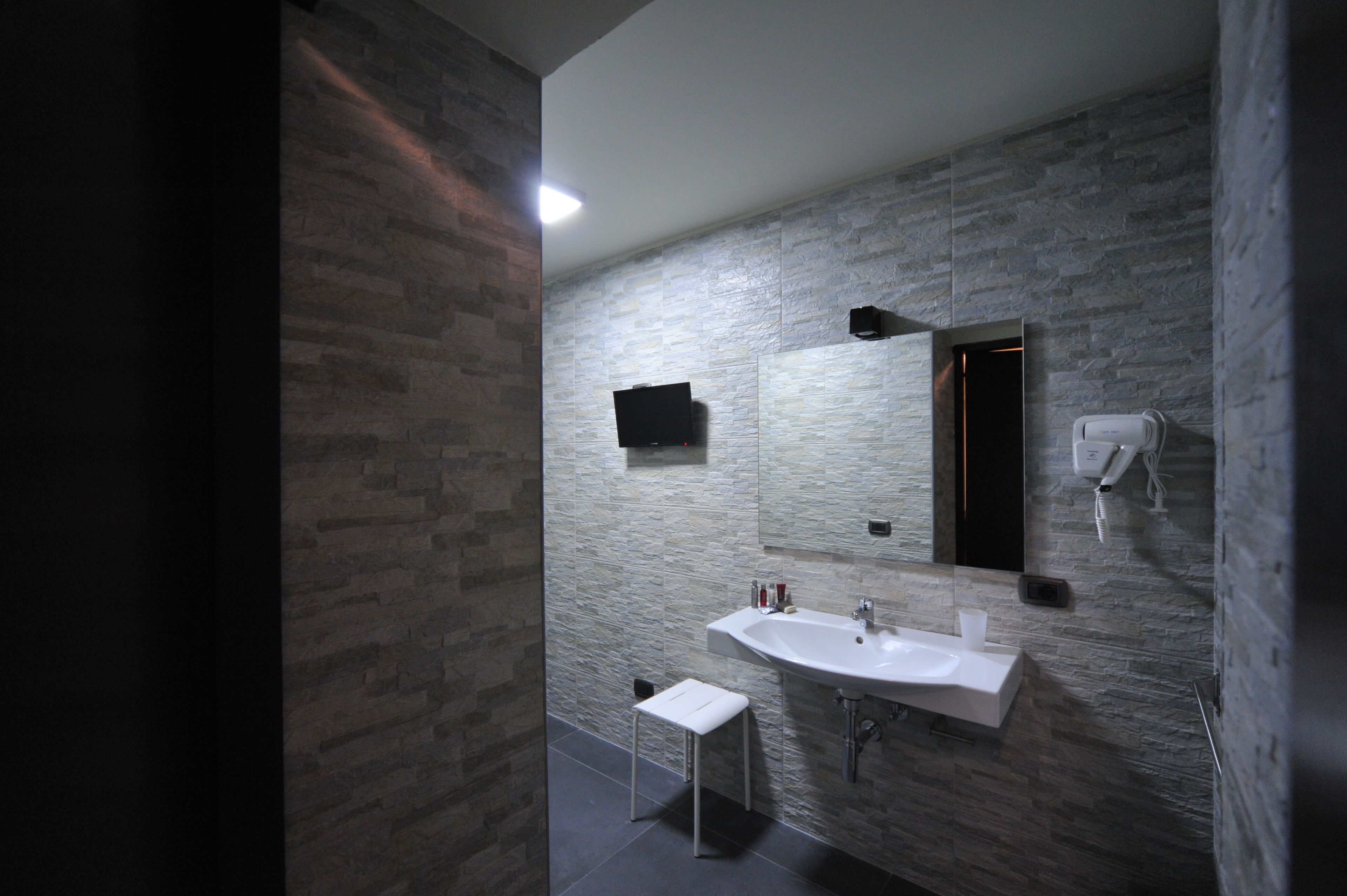 A modern bathroom with a stone-textured wall, a large mirror, a sink, and a hairdryer.