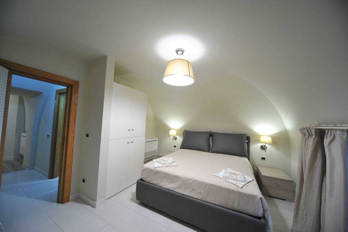 A bedroom with a large bed, a wardrobe, a nightstand, and a ceiling light.