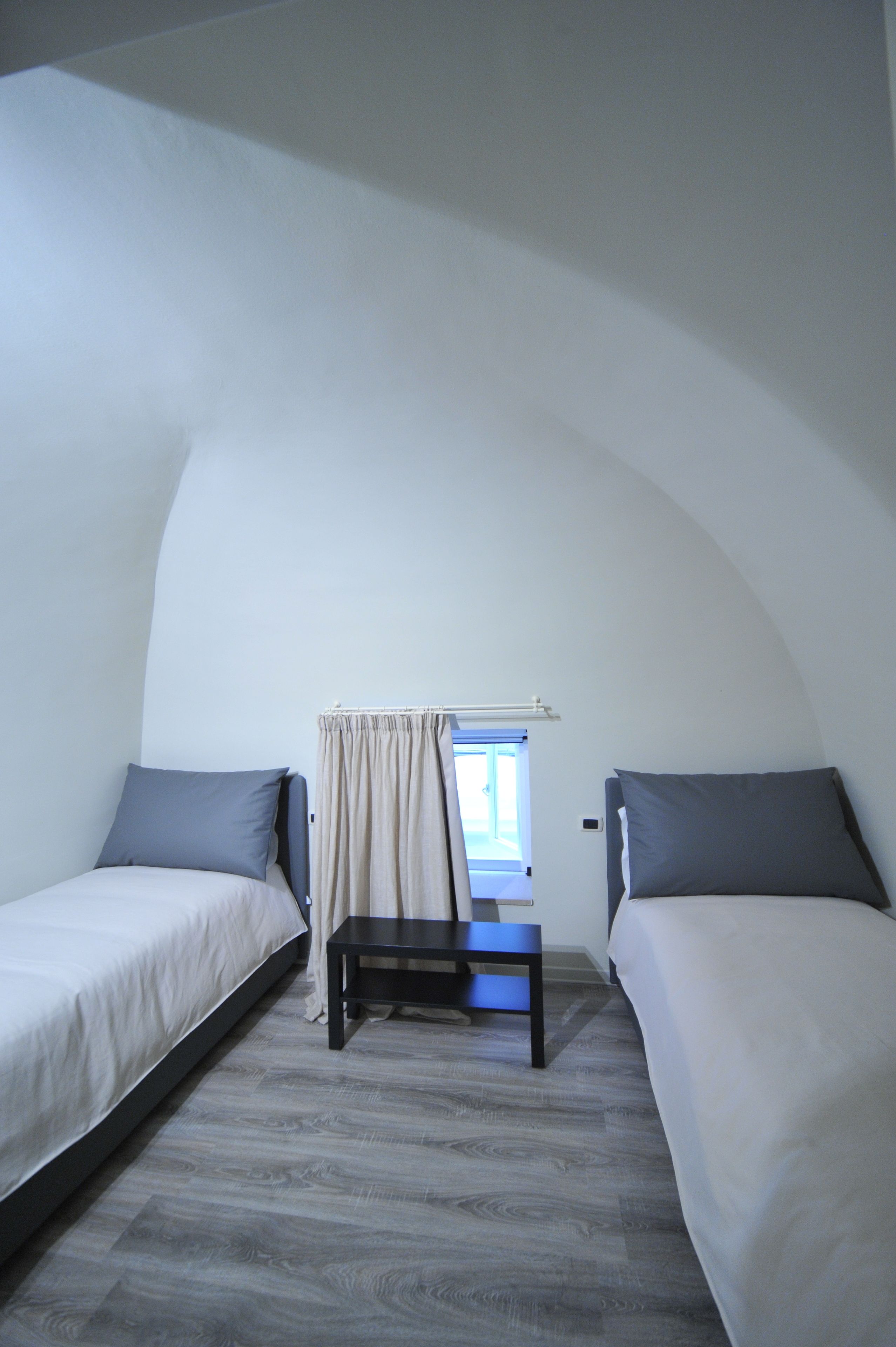 Een kleine eenpersoons slaapkamer met twee bedden, een nachtkastje en een raam met gordijnen.
