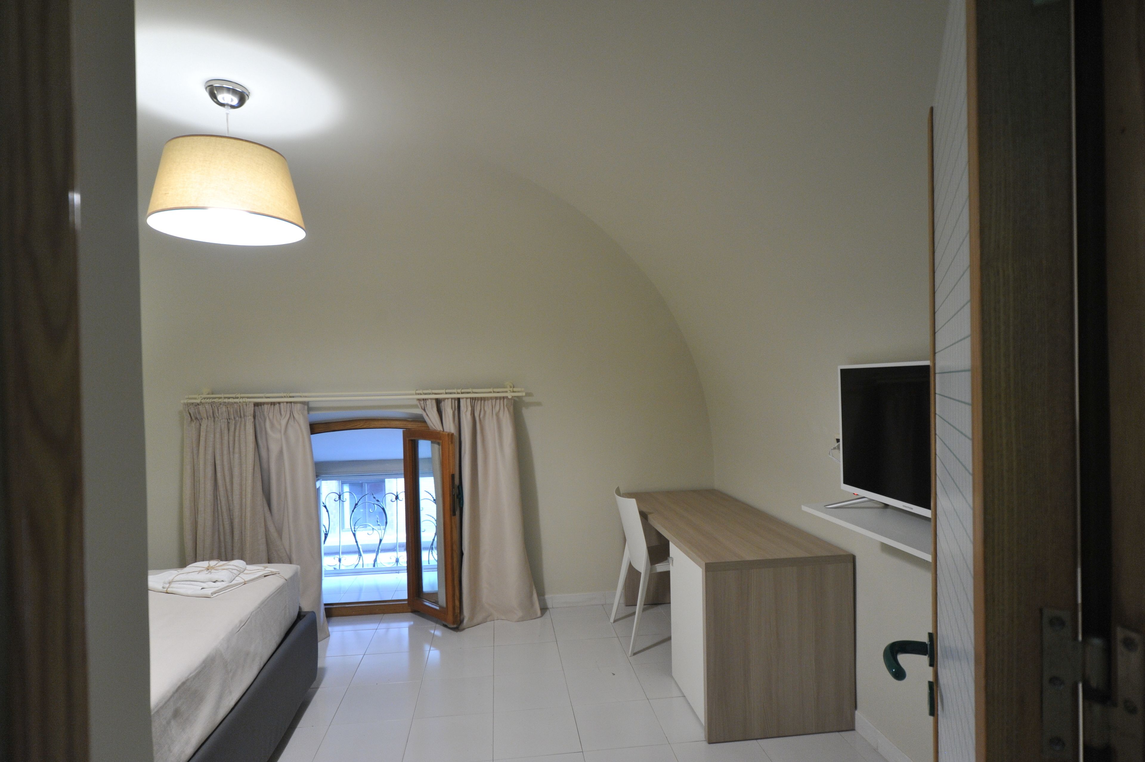 Un dormitorio con cama, escritorio, televisión y vistas al exterior.