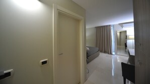 A hotel room with a bed, a desk, and a chair. There is a door and a window with curtains.