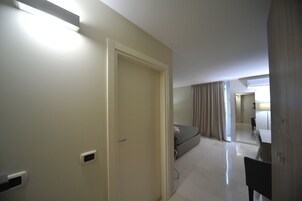 A hotel room with a bed, a desk, and a chair. There is a door and a window with curtains.