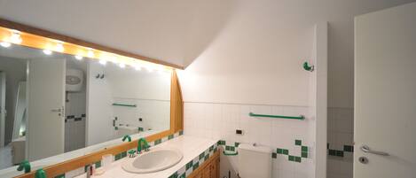 A bathroom with two sinks, a toilet, and a mirror with lights.