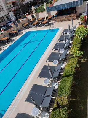 Ein Pool mit Liegestühlen und Sonnenschirmen, umgeben von Grünflächen und Gebäuden.