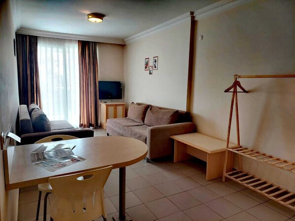 Un espace de vie compact comprenant un canapé, une petite table, un téléviseur et un porte-manteau.