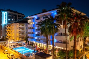 Un hôtel  à plusieurs étages doté d’une piscine, d’un espace extérieur aménagé et de palmiers.
