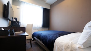 A hotel room with a bed, a desk, a chair, a television, and a window with curtains.