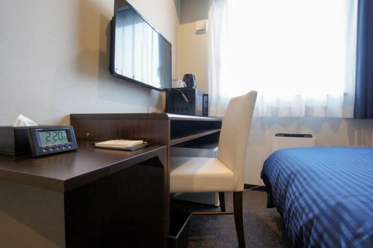 Hotellihuone, jossa on työpöytä, tuoli, sänky ja seinälle asennettu televisio.