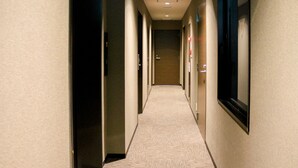 A hotel hallway with carpeted floors, doors on both sides, and a light fixture on the ceiling.
