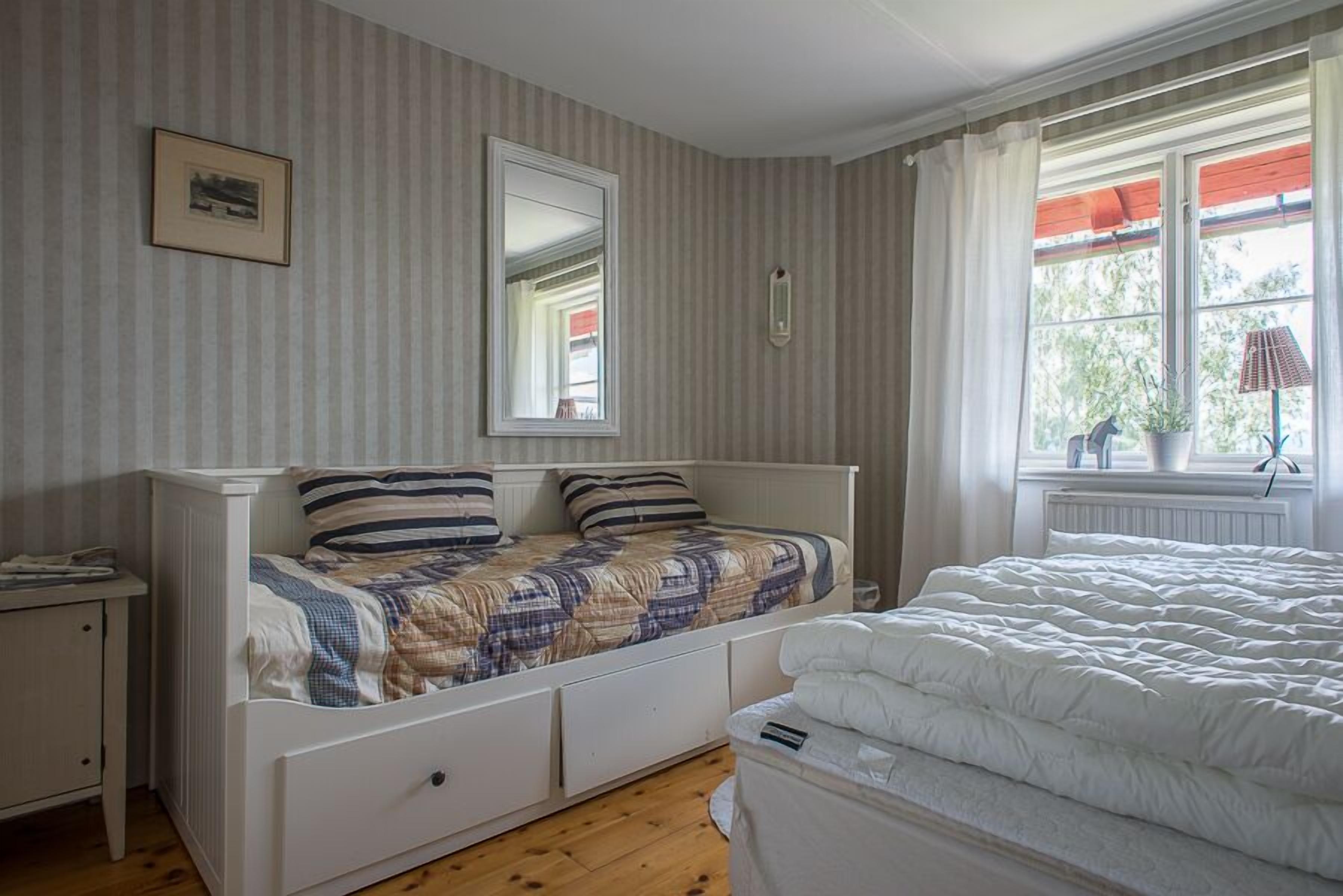 A bedroom with a bed, a nightstand, a dresser, a window with curtains, and a radiator.