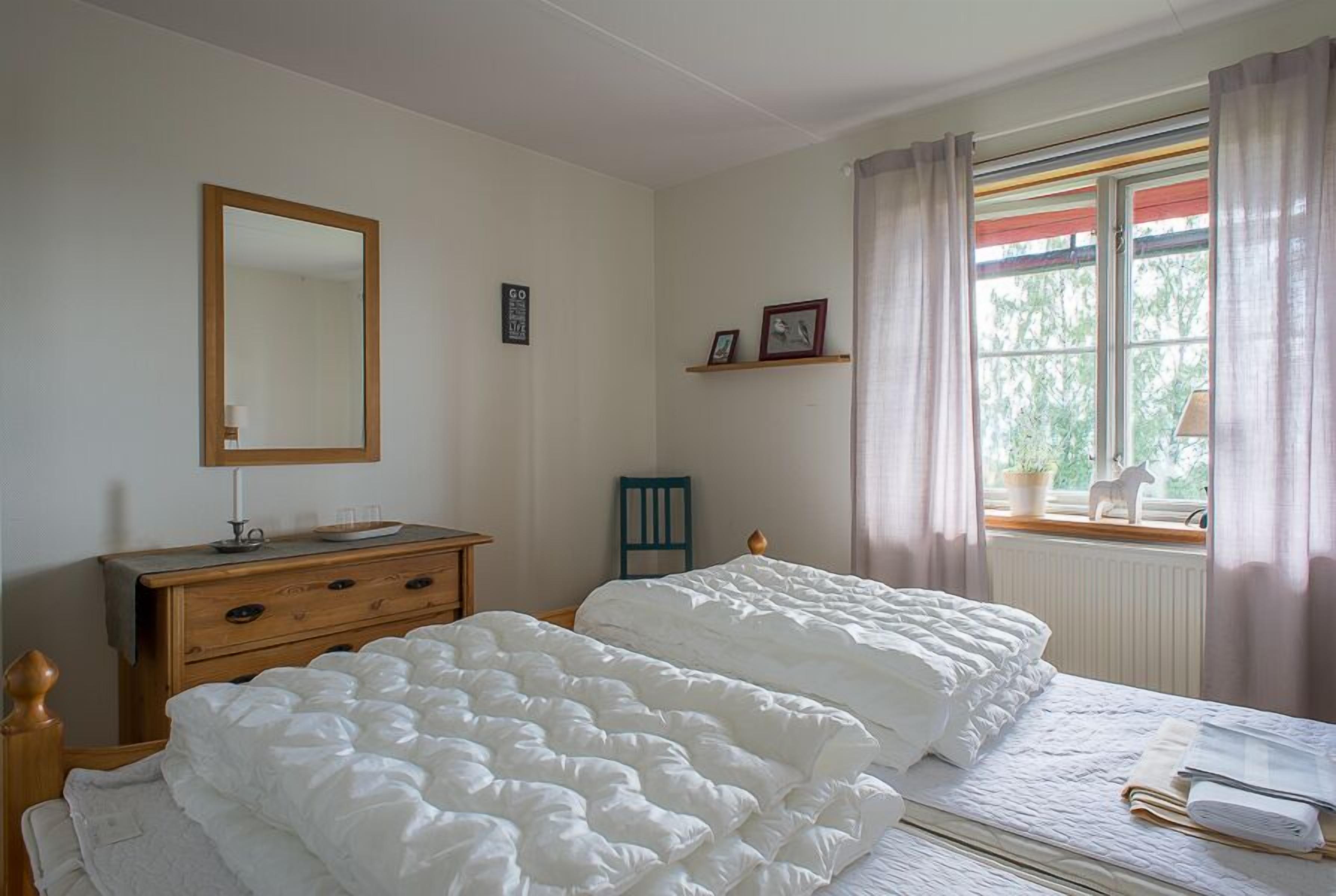 A bedroom with two beds, a dresser, a mirror, and a window with curtains.