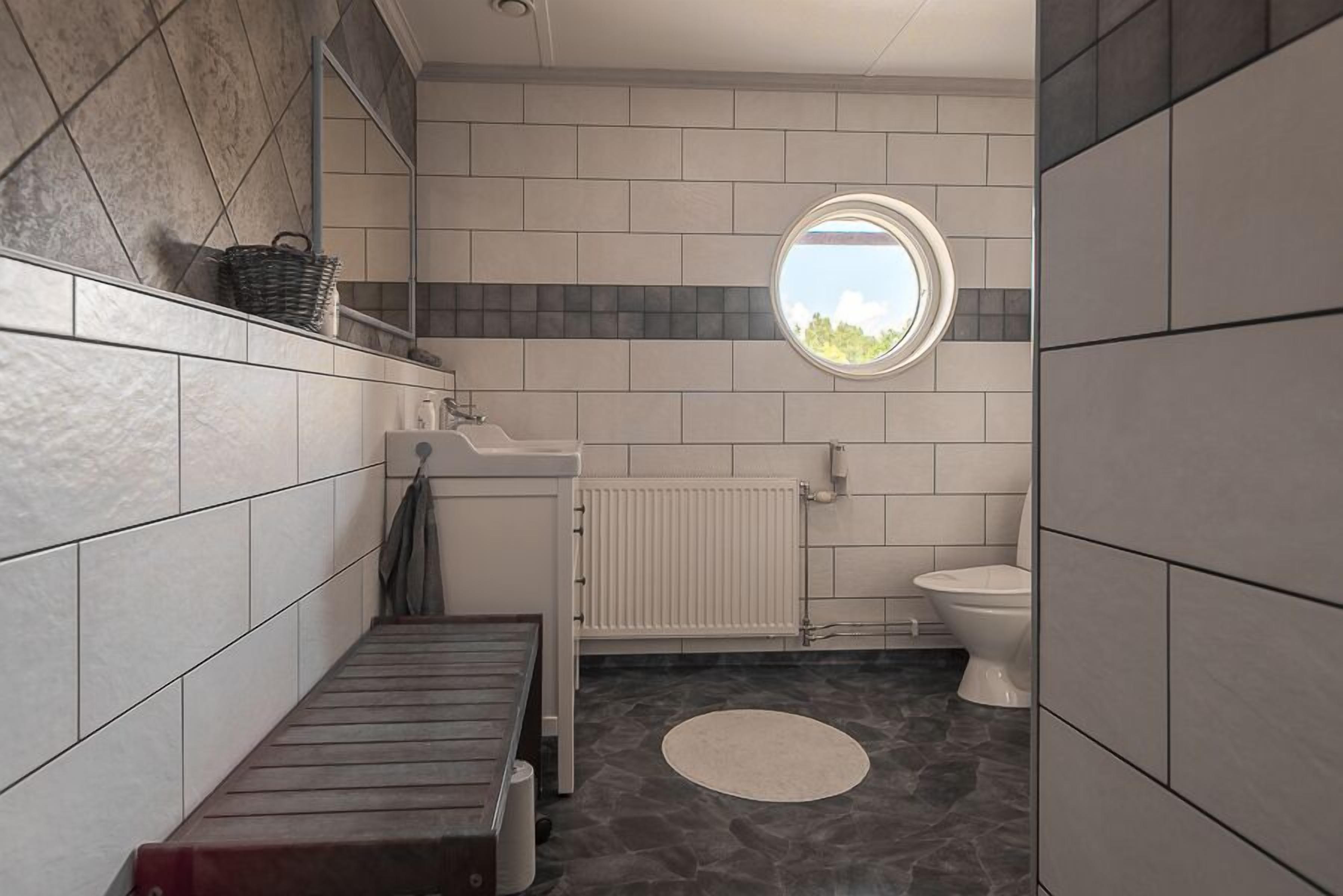 A bathroom with a bathtub, a toilet, a sink, a window, and a circular mirror.