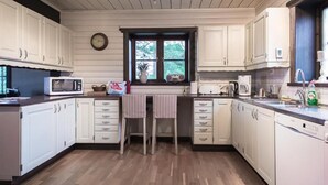 Una cocina con armarios blancos, microondas, cafetera y ventana con vista a follaje.