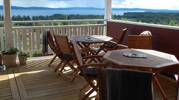 Una terraza de madera con una mesa y sillas, con vistas a un lago y una zona boscosa.