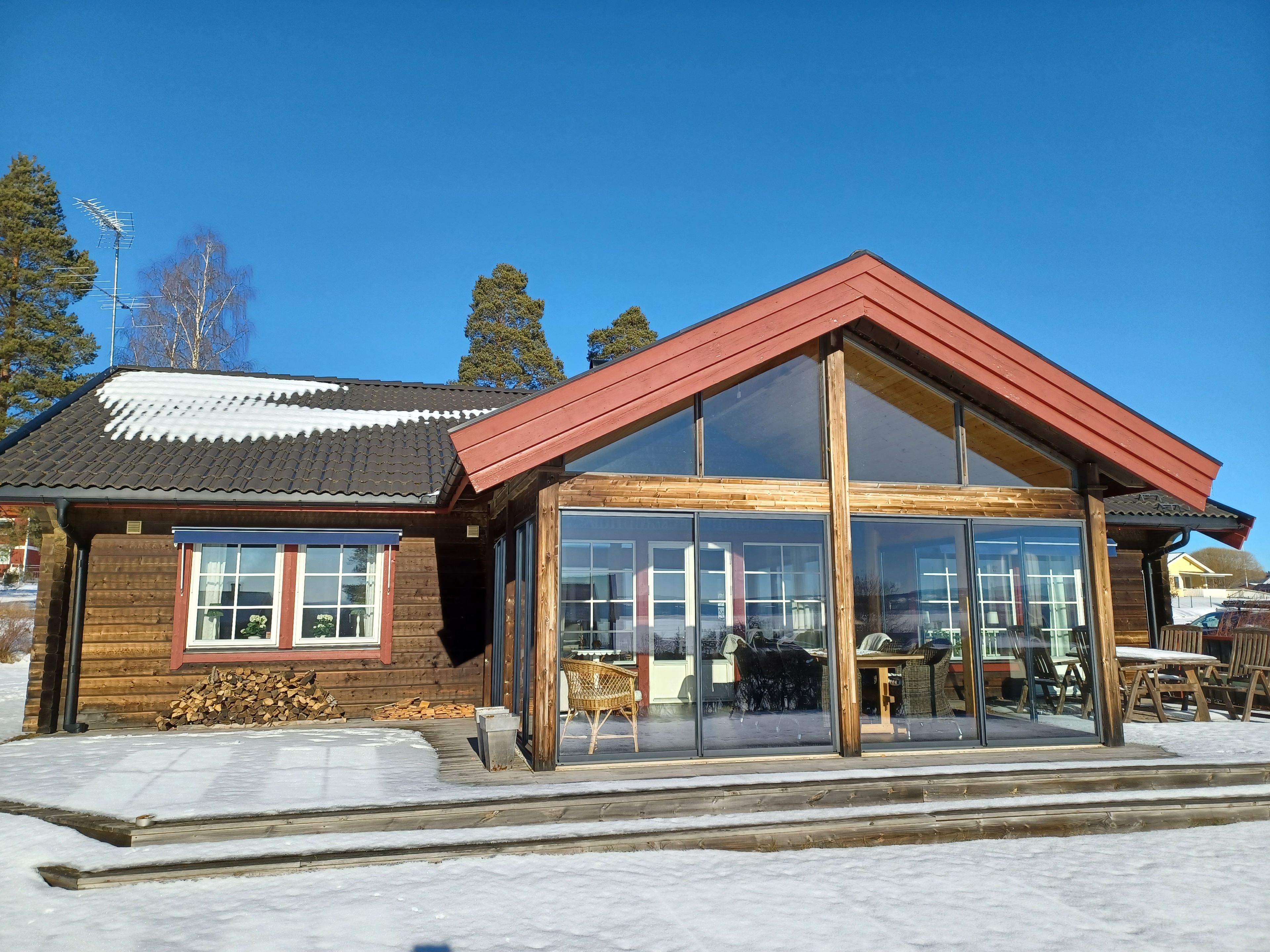 Une cabane en bois dotée de grandes fenêtres en verre et d’un toit rouge.