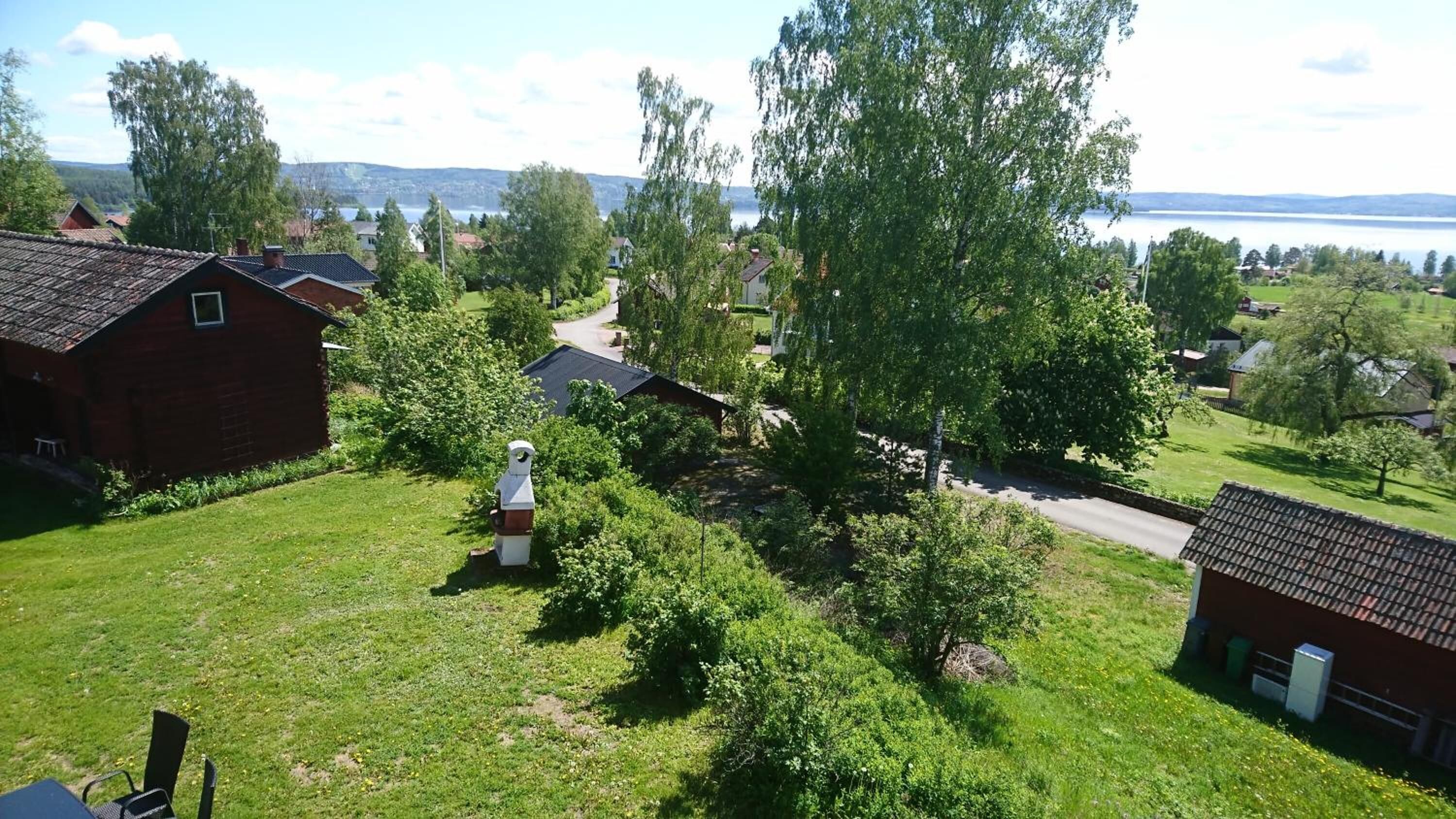 En lantlig miljö med hus, en väg och en vattenyta i bakgrunden.