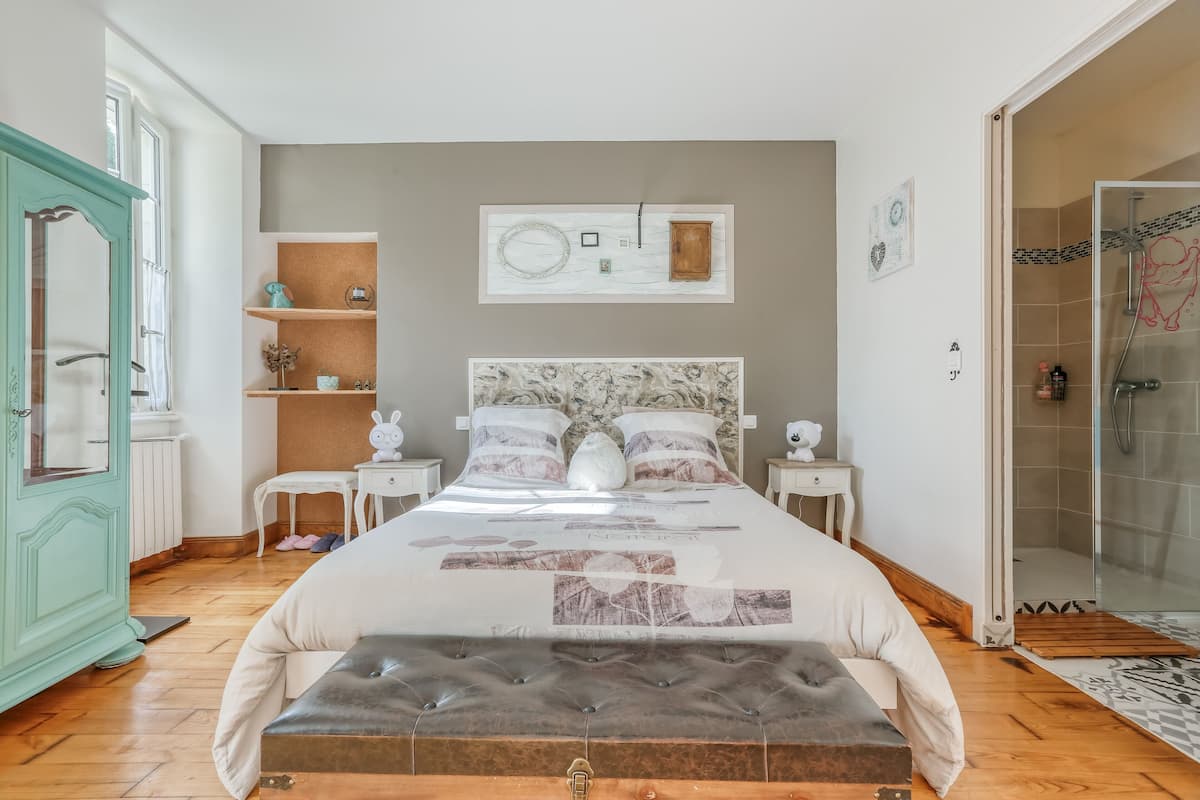 A bedroom with a large bed, a bench, a wardrobe, and a shower area.