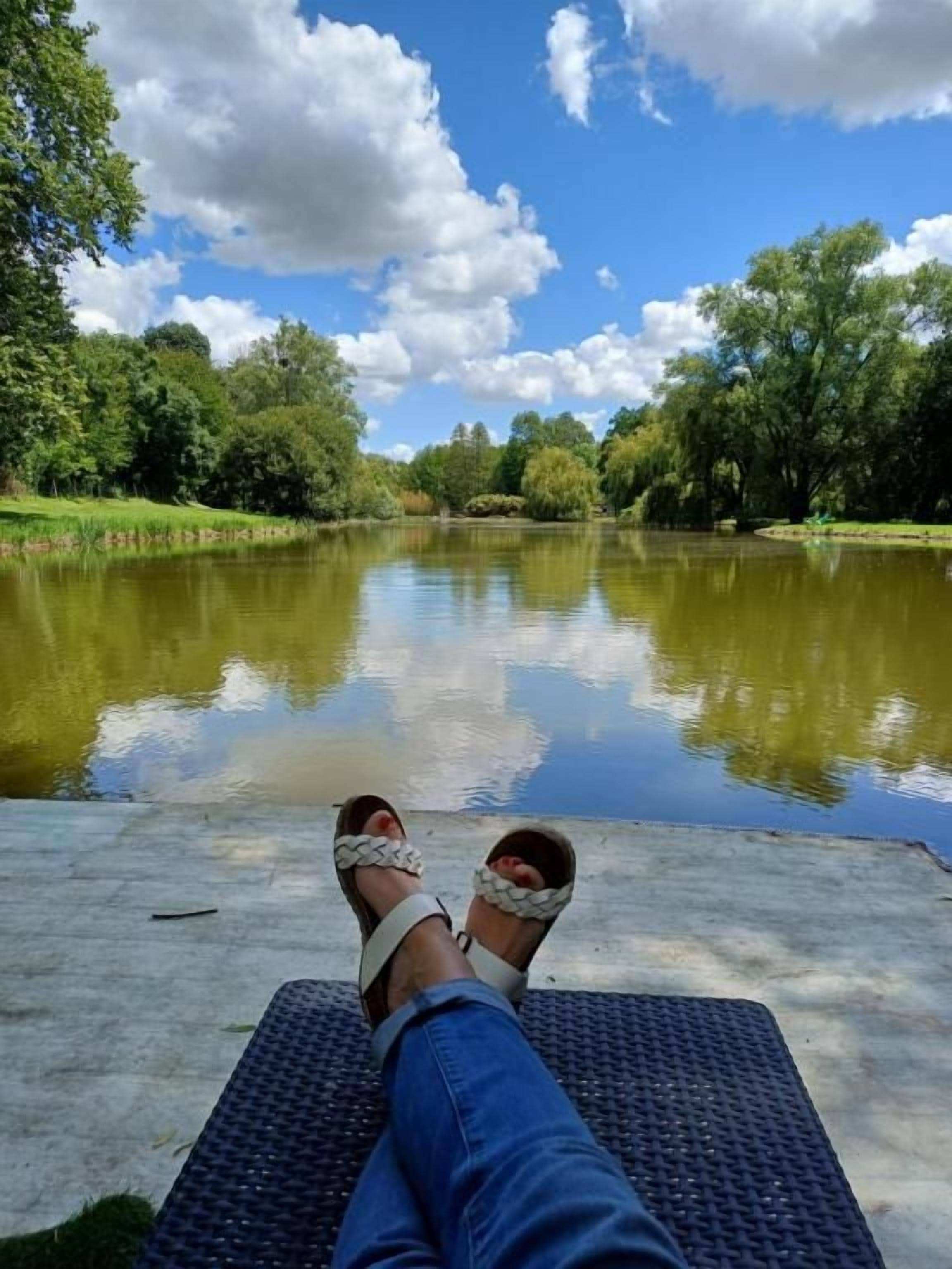Une personne allongée sur un tapis au bord d’un lac paisible, avec des arbres en arrière-plan.