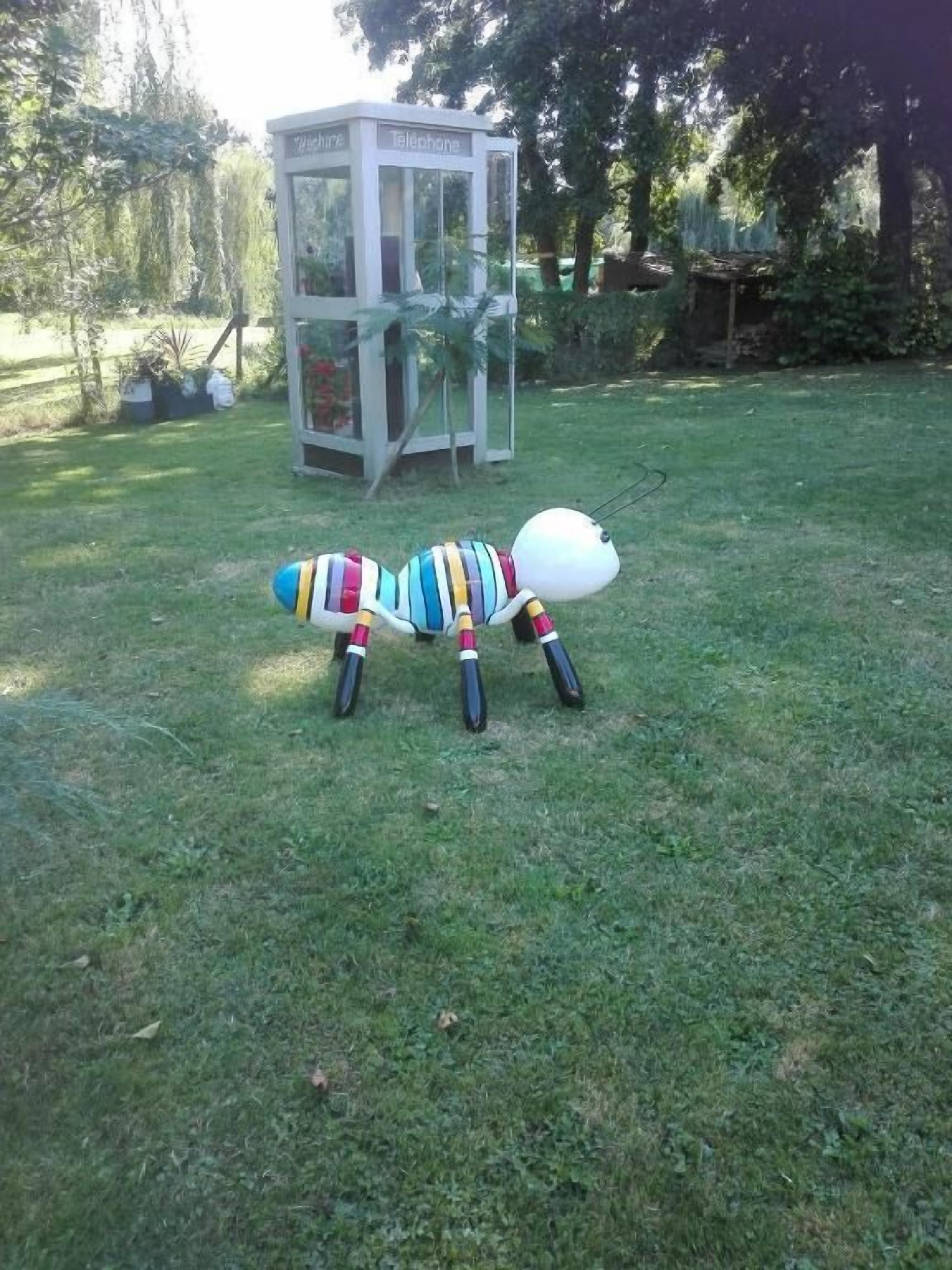 A colorful toy ant on a grassy lawn with a telephone booth in the background.