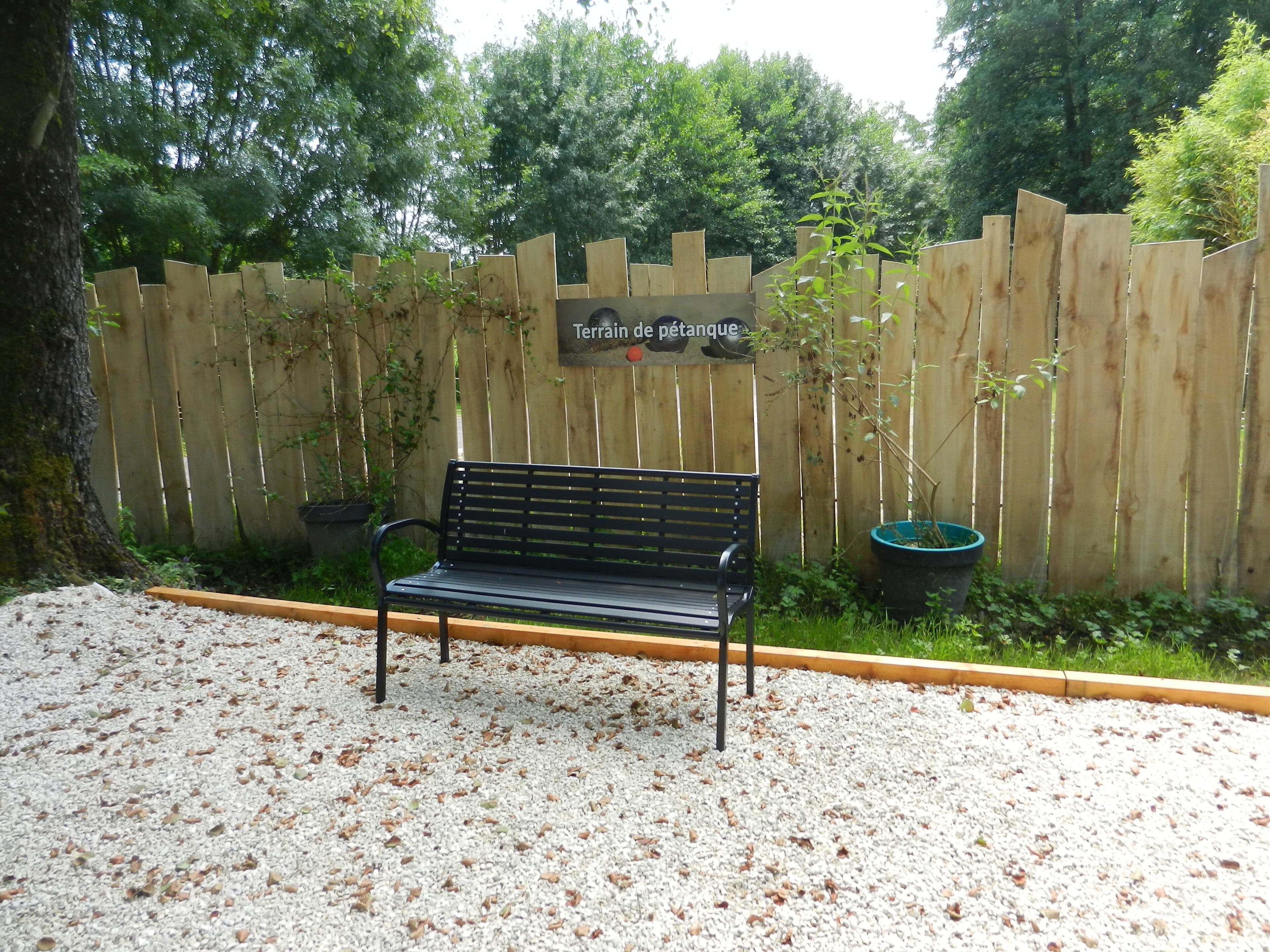 Un banco en un área de jardín con una cerca de madera y un letrero que dice 'Terrain de pétanque'.