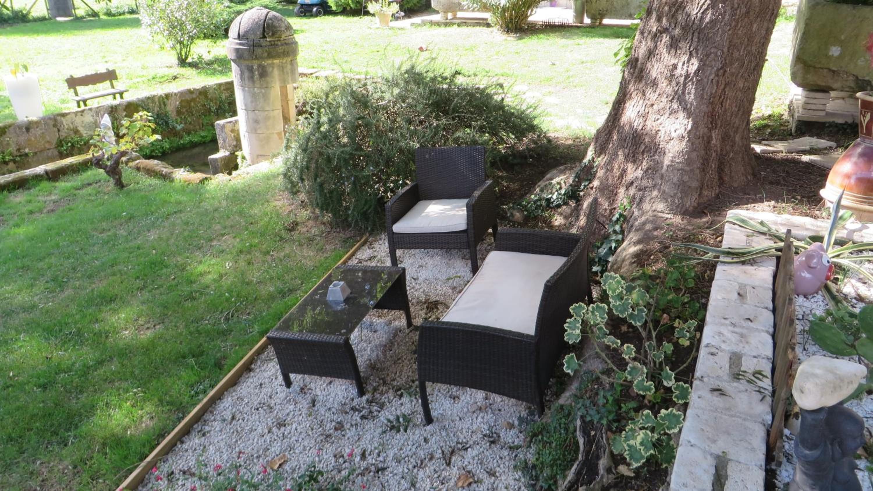 Un patio con mobiliario de mimbre, un pilar de piedra y un árbol.