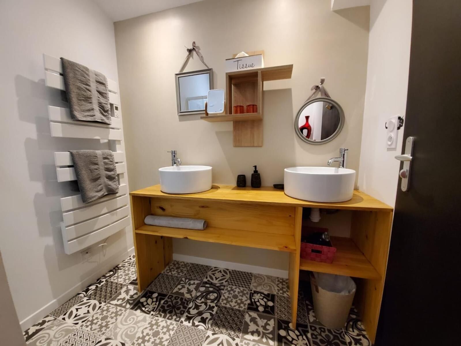 Un baño moderno con dos lavamanos, un espejo, un perchero para toallas y un estante con artículos de aseo.