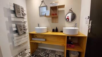 A modern bathroom with two sinks, a mirror, a towel rack, and a shelf with toiletries.