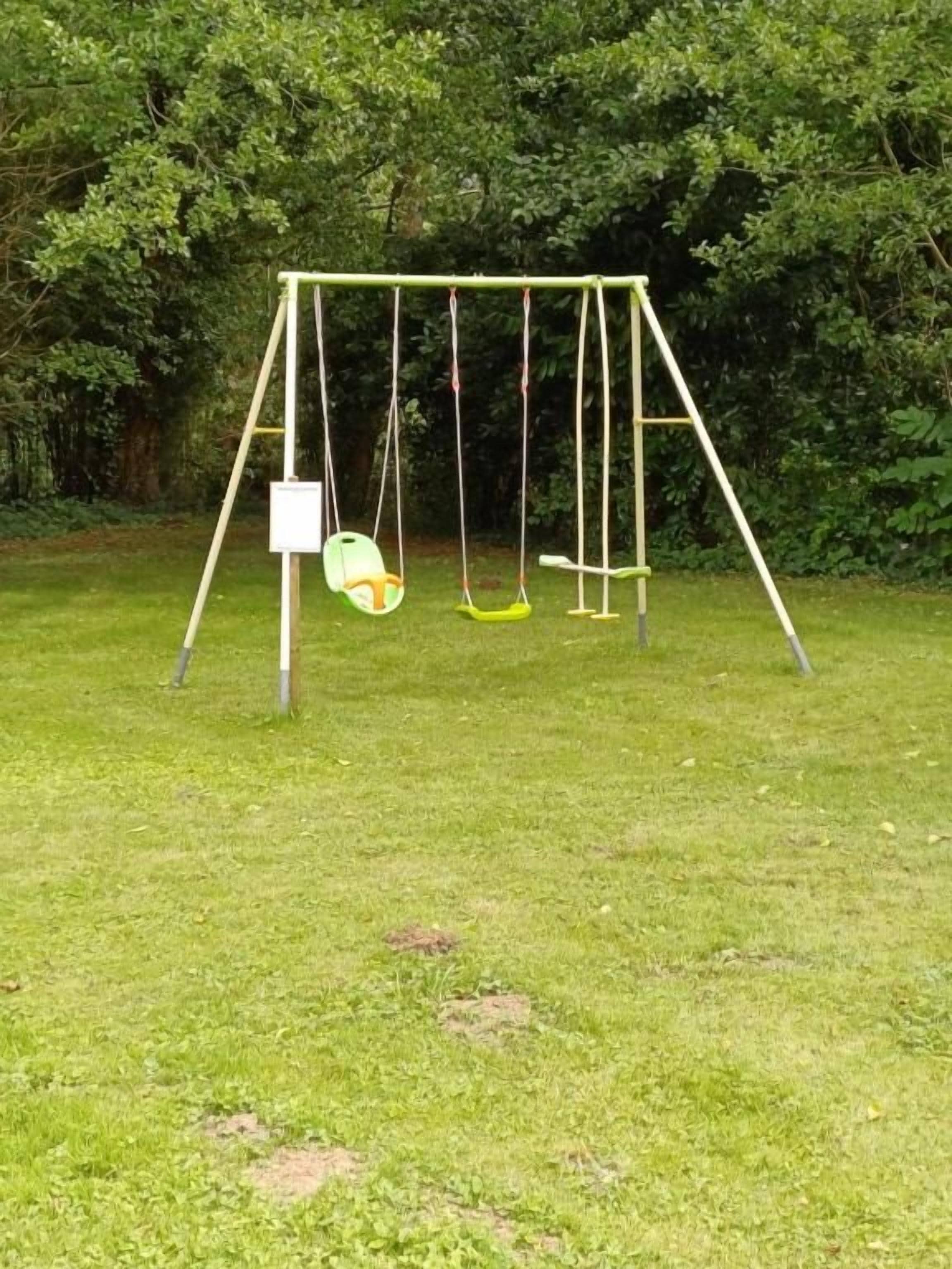 A swing set in a grassy area with trees in the background.