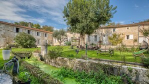 A courtyard with stone buildings, a tree, a water feature, and outdoor seating. - Jolysable (Pons)