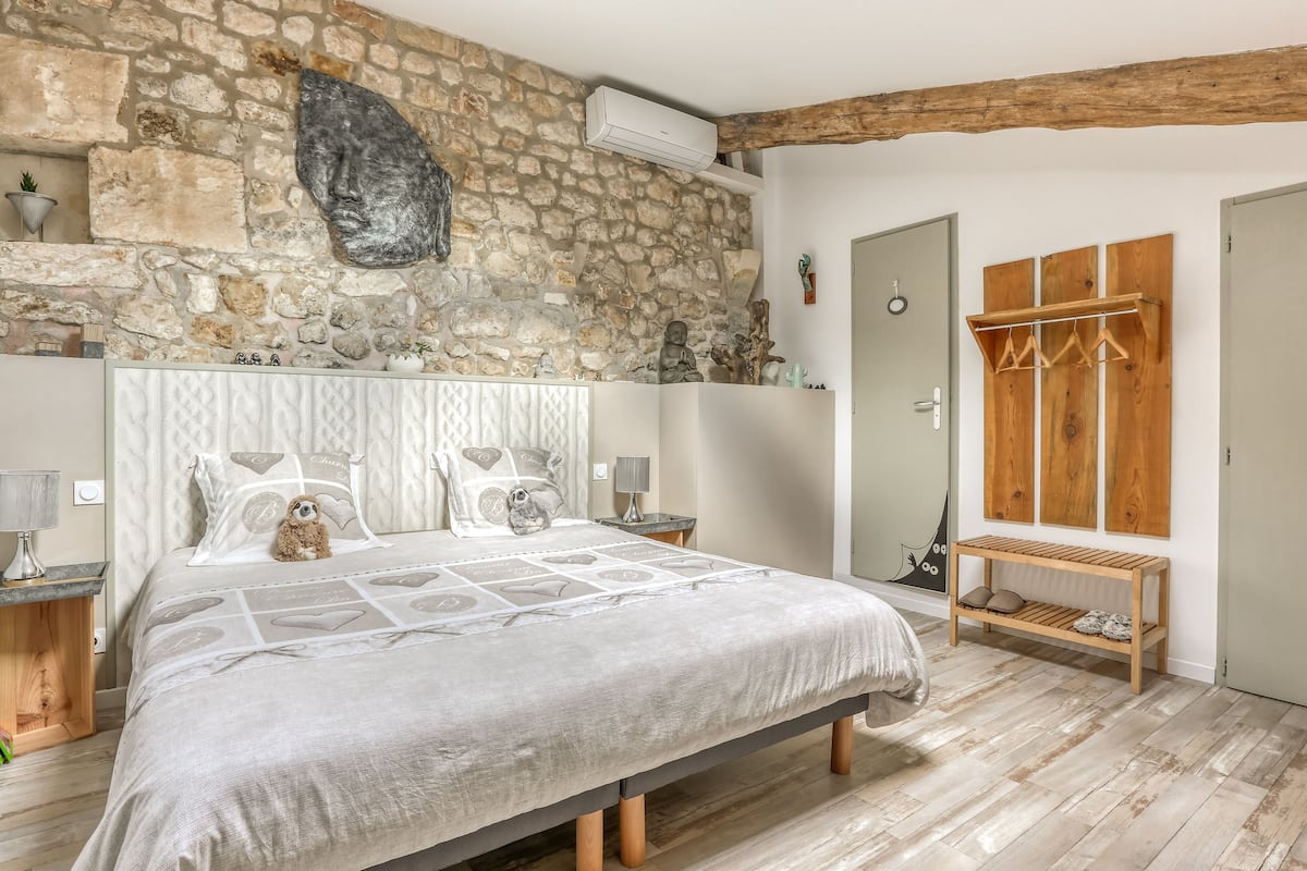 A bedroom with a stone wall, a bed with patterned bedding, a wooden bench, and a coat rack.