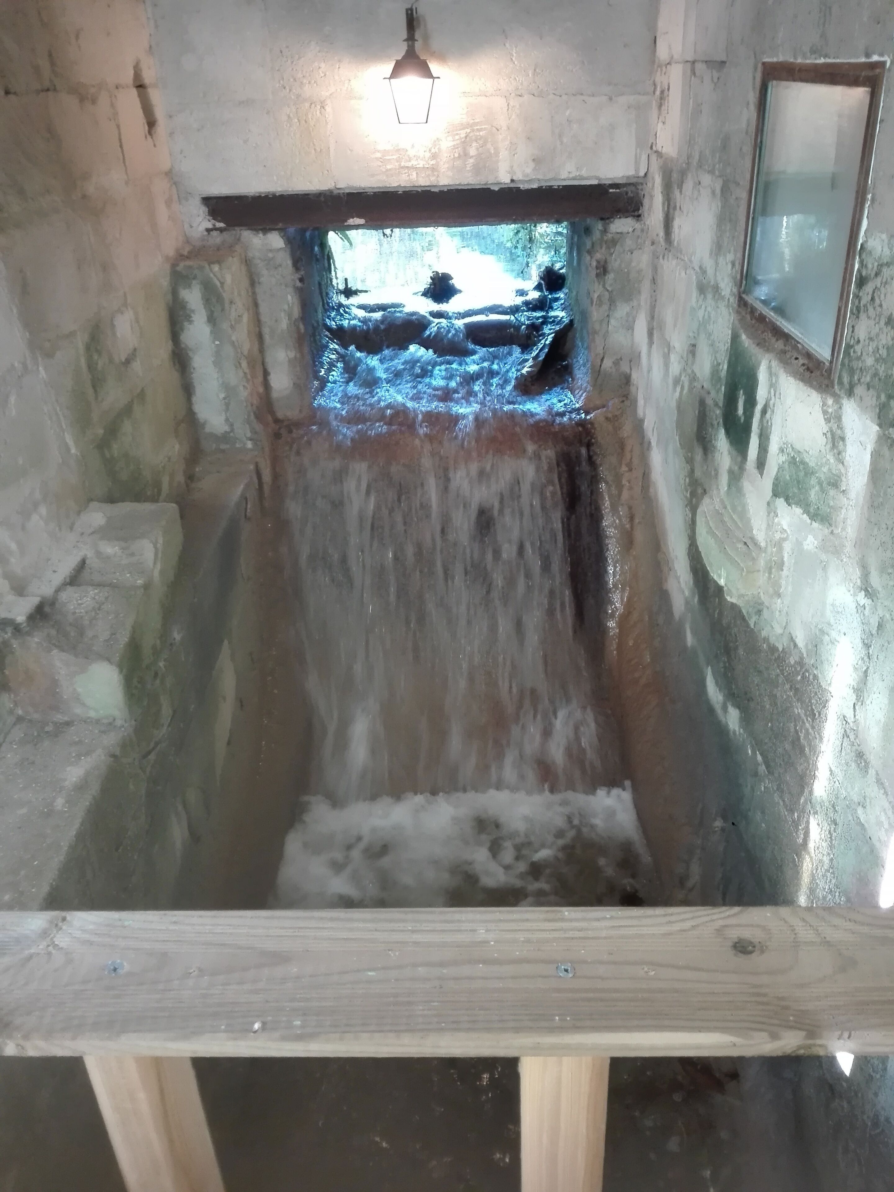 Una habitación con paredes de piedra, un banco de madera y un ventanal en la parte superior.