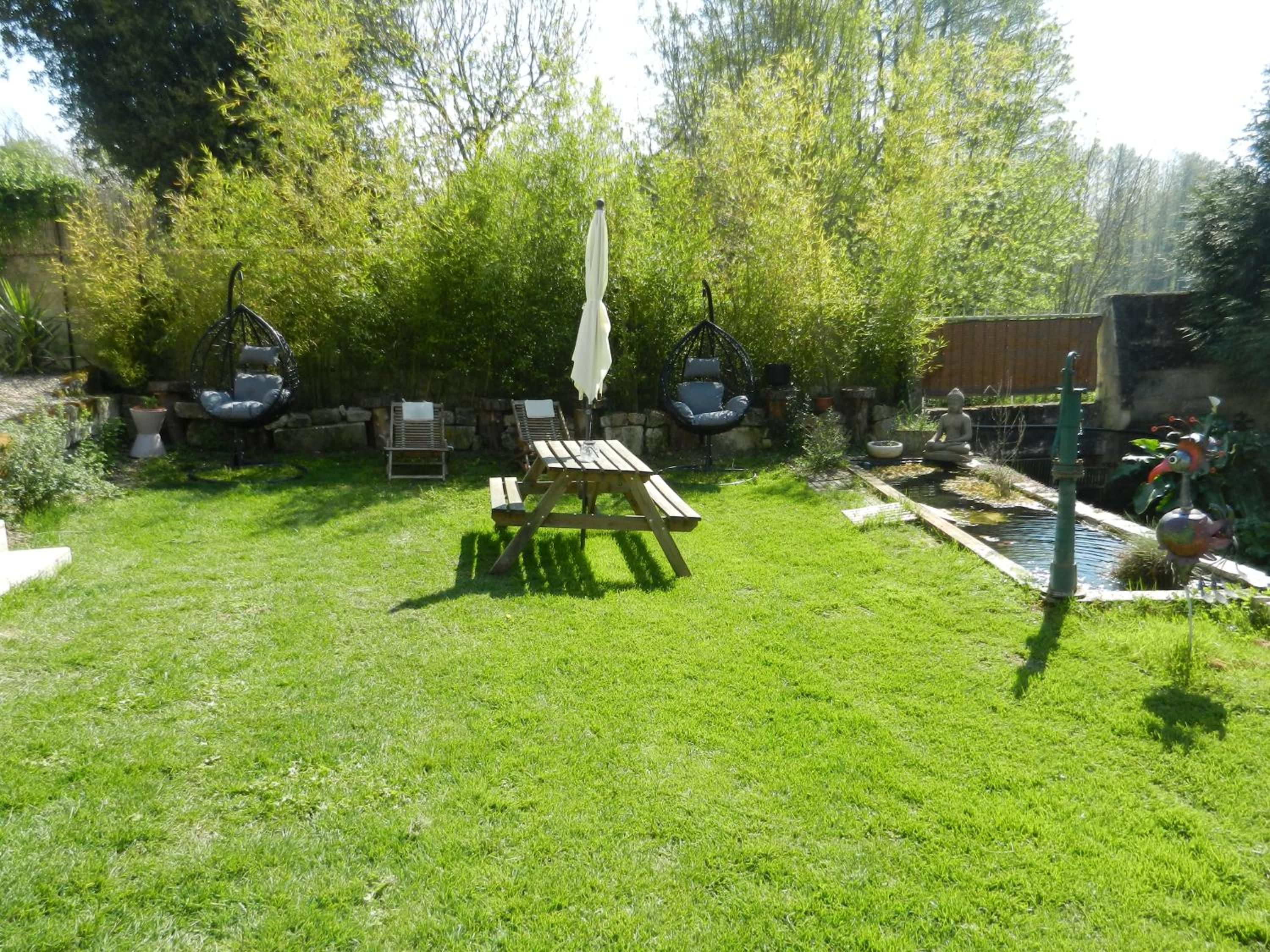 A backyard with a wooden picnic table, two hanging chairs, a small pond, and a statue.
