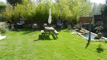 A backyard with a wooden picnic table, two hanging chairs, a small pond, and a statue.