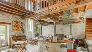 A rustic interior with a stone bar, wooden beams, and a high ceiling. - Jolysable (Pons)