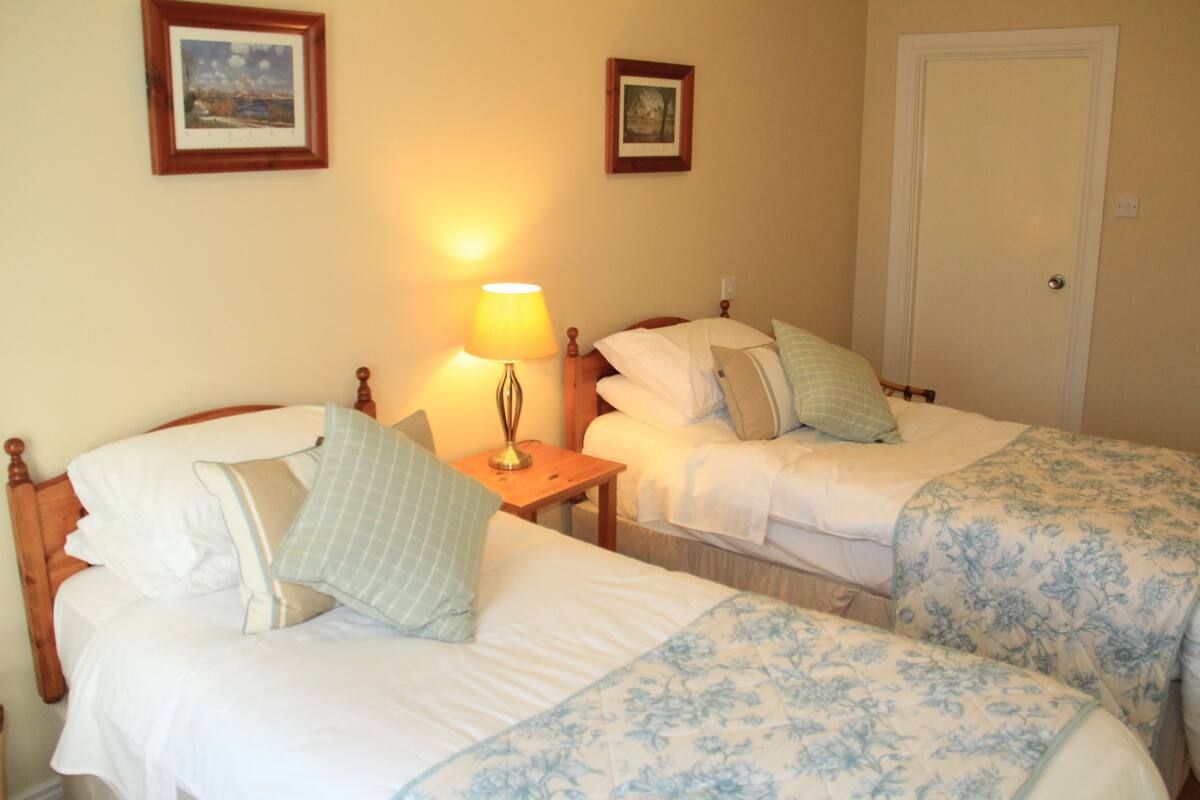 A room with two single beds, a nightstand with a lamp, and two framed pictures on the wall.