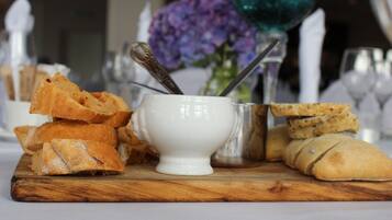 A wooden board with various food items, including bread and a white ceramic bowl with a spoon.