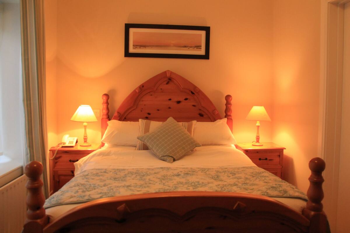 A neatly made bed with a wooden headboard, two bedside lamps, and a framed picture on the wall.