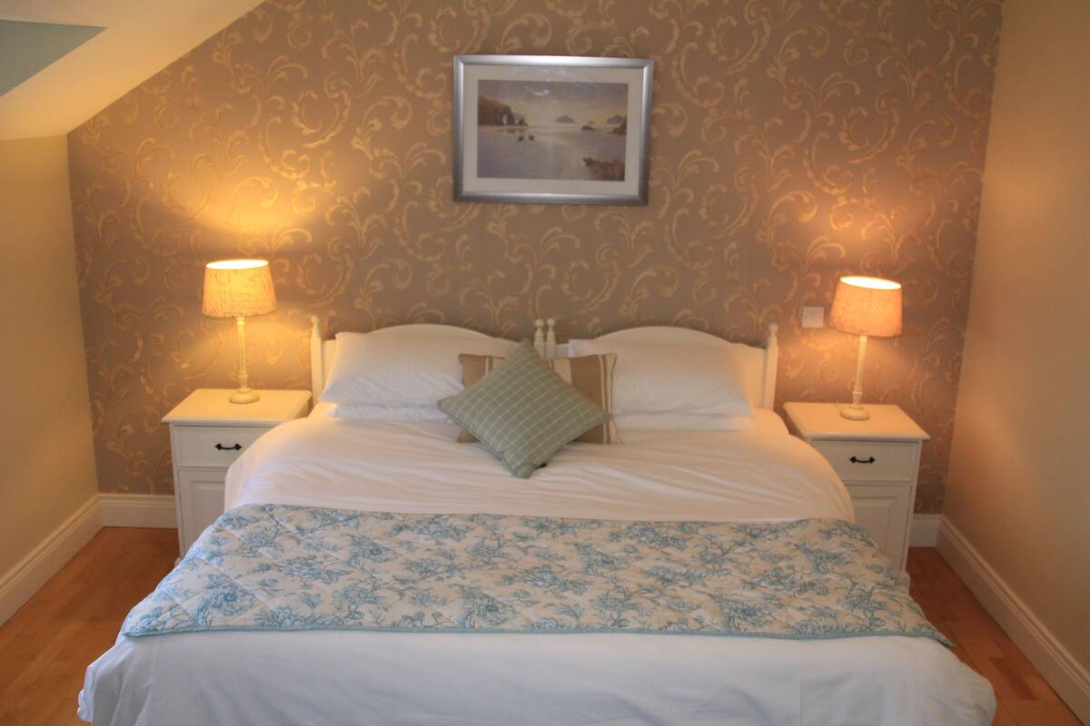 A neatly made bed with a floral bedspread, two bedside lamps, and a framed picture on the wall above the bed.