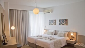 Une chambre d’hôtel avec deux lits, un bureau, une chaise et une grande fenêtre avec des rideaux.