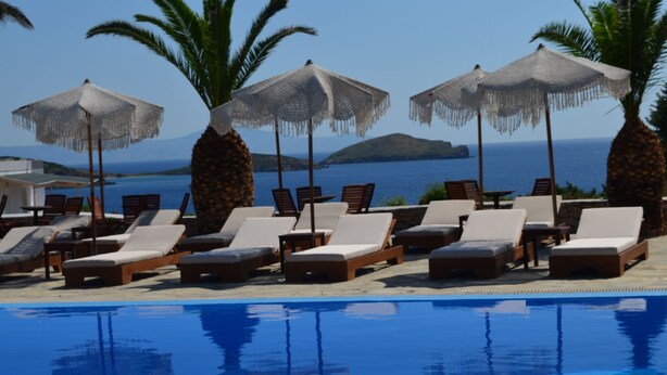 Un espace aménagé au bord de la piscine, avec des chaises longues et des parasols, donnant sur une étendue d’eau.