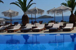 Ein Poolbereich mit Liegestühlen und Sonnenschirmen mit Blick auf ein Gewässer.