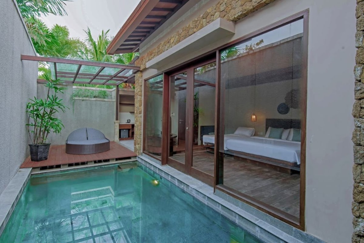 Un espace piscine privatif comprenant une chambre avec murs en verre et un coin salon doté d’un banc rembourré.