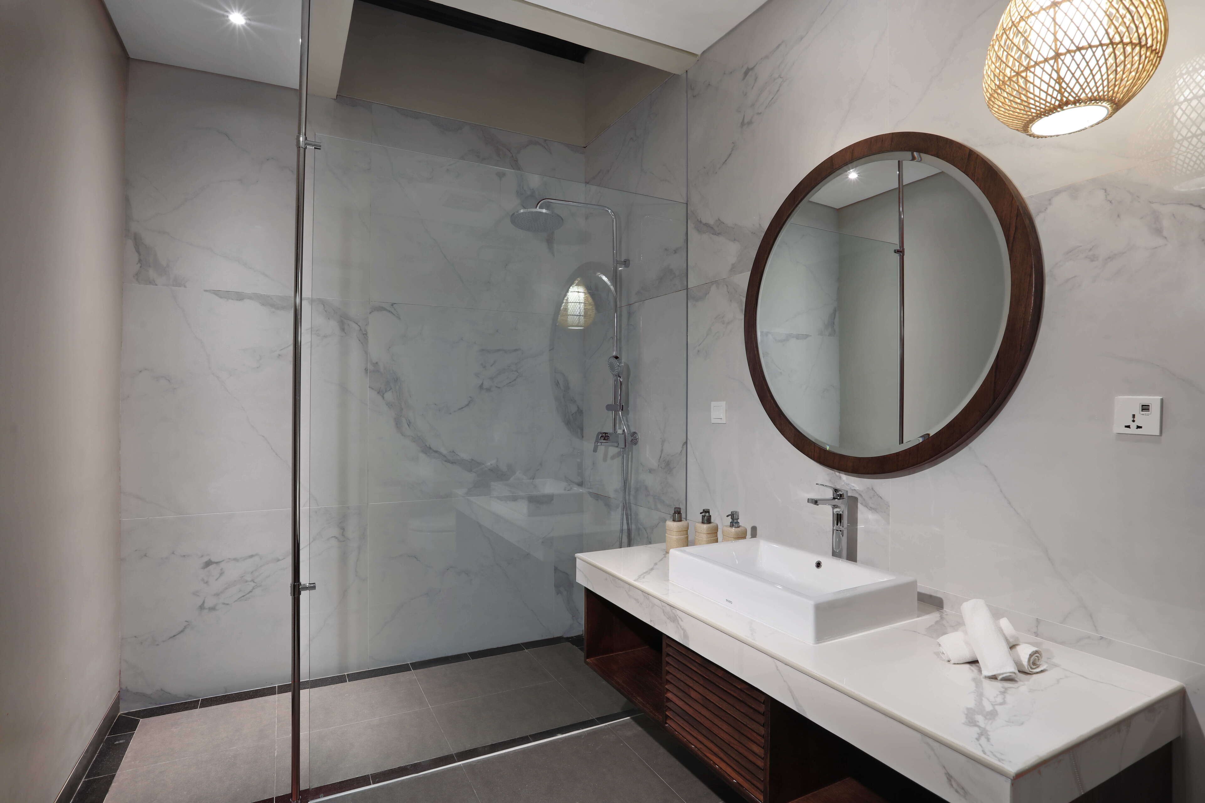 Un baño moderno con ducha envuelta en vidrio, un espejo grande y un tocador blanco con encimera de mármol.