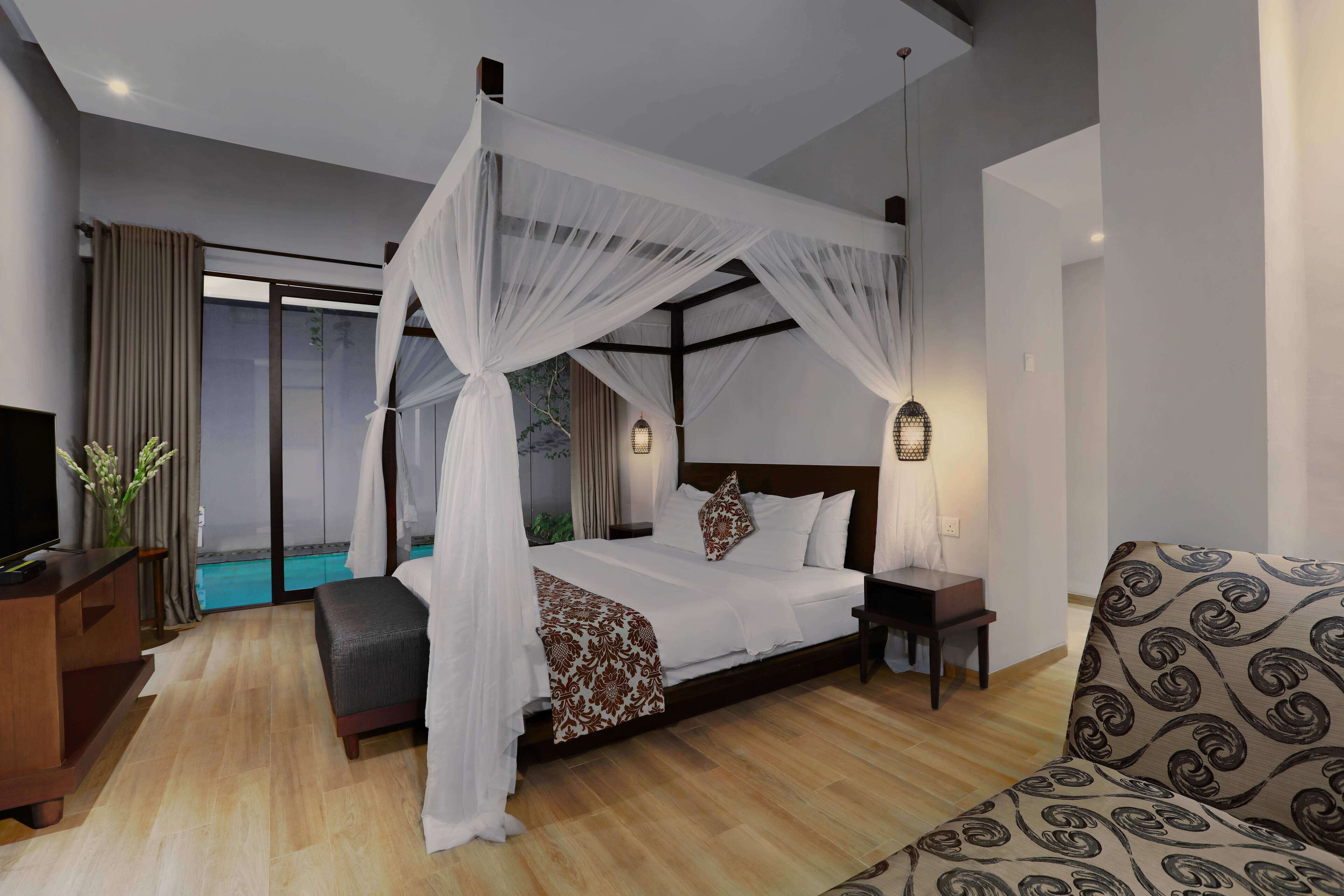 A bedroom with a four-poster bed, a sofa, a TV, and a view of a pool.