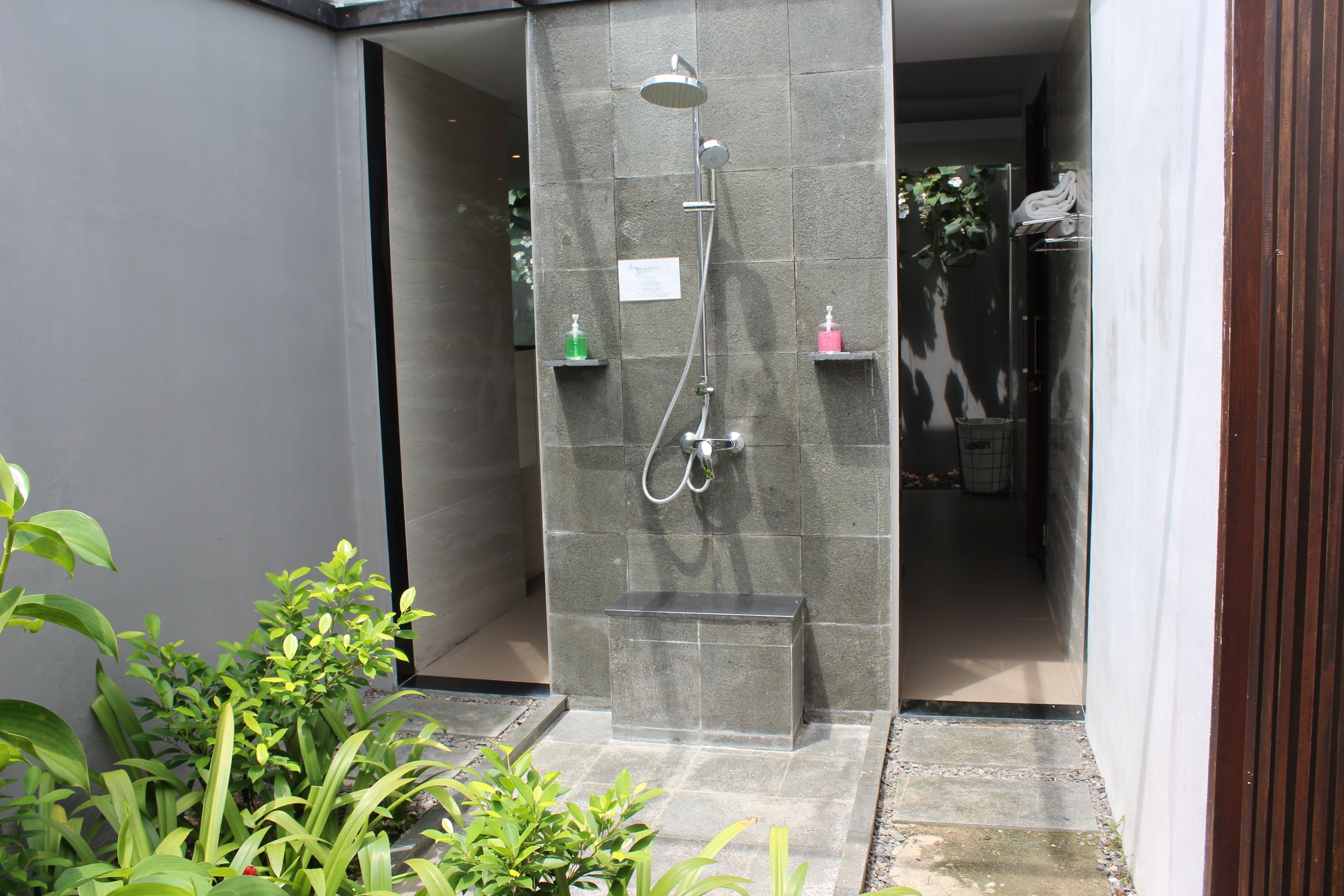 A modern shower enclosure with a built-in bench, a handheld showerhead, and two soap dispensers on wall-mounted shelves.