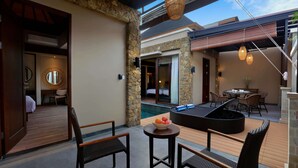 A modern outdoor seating area with wicker furniture, a stone wall, and a pool in the background. - Kamuela Villas Lagoi Bay Bintan (Bintan)