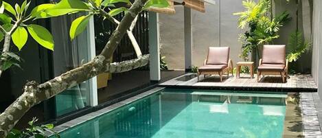 A swimming pool with clear water, surrounded by lush greenery and a modern house.