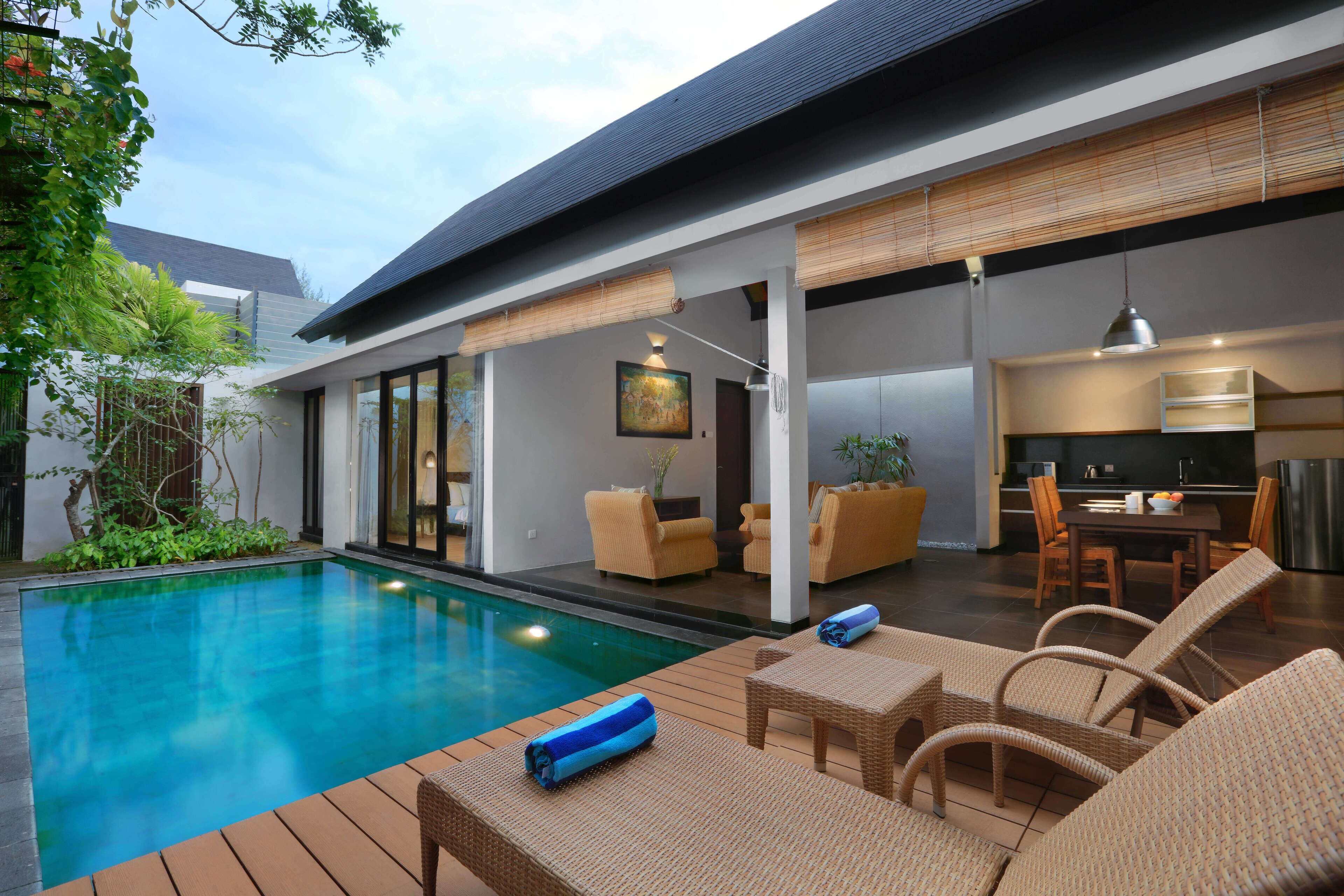 Un espace piscine extérieur moderne, doté de chaises longues et d’une table à manger.