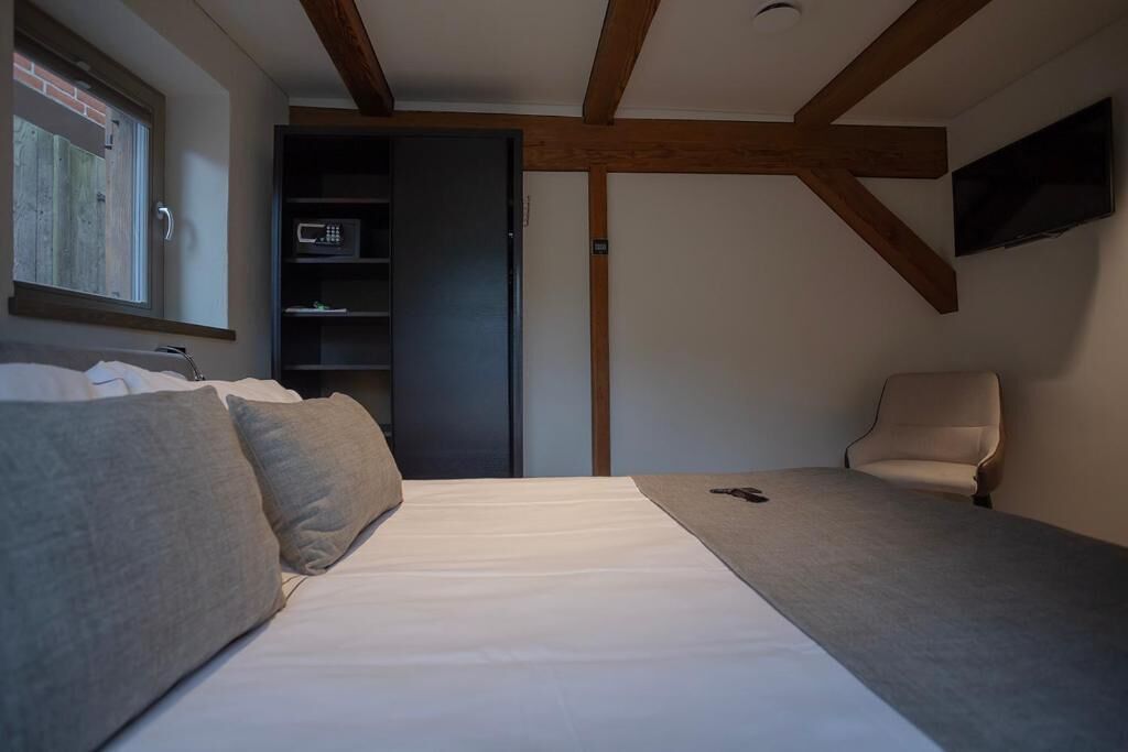 A bedroom with a bed, a chair, a TV, and a shelf with a microwave.