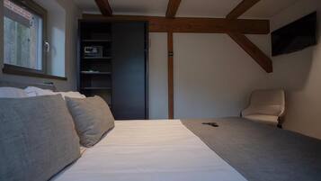 A bedroom with a bed, a chair, a TV, and a shelf with a microwave.